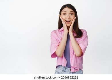 Portrait Of Cute Girl Gasp And Look Surprised, Saying Wow, Looking With Amazement At Camera, Standing Over White Background