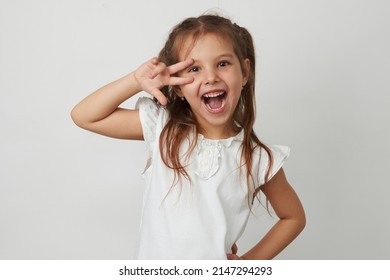 Portrait of cute girl give v-sign near eye. Smiling little girl posing over white background with copy space, close-up
