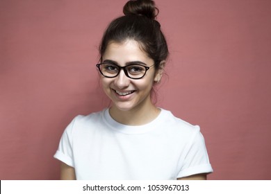 Portrait of a cute girl with glasses smiling looking into the camera. A happy young indian woman is happy standing on a red background. - Shutterstock ID 1053967013