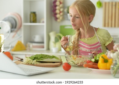 Portrait of cute girl making salad on kitchen and using laptop