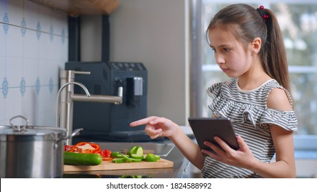 Portrait of cute girl preparing salad and using tablet reading recipe. Attractive teen girl searching for vegetable meal recipe in tablet pc preparing dinner in kitchen at home - Powered by Shutterstock