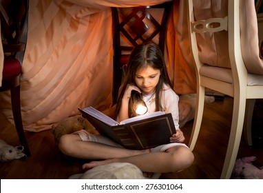 Portrait of cute girl sitting under blanket and reading a book