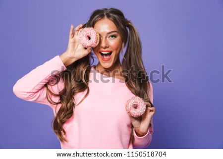 Portrait of a cute girl in sweatshirt posing with donuts isolated over violet background