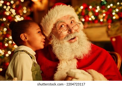 Portrait of cute  girl whispering secrets to Santa Claus on Christmas eve - Shutterstock ID 2204723117