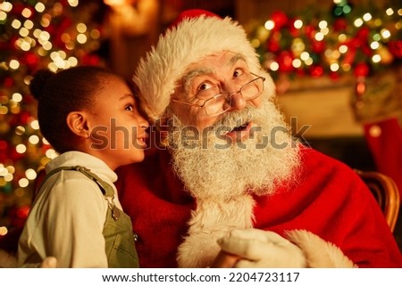 Portrait of cute  girl whispering secrets to Santa Claus on Christmas eve