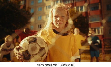 Portrait of a Cute Girl in Yellow T-Shirt Holding a Soccer Ball on a Field in the Neighborhood. Young Female Football Player Looking at Camera, Smiling. Concept of Sports, Childhood, Friendship. - Powered by Shutterstock