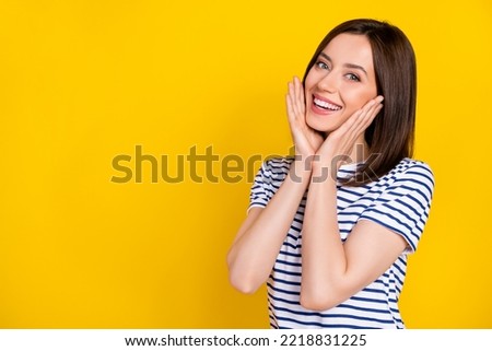 Portrait of cute gorgeous girl straight hairstyle wear striped t-shirt palms on cheekbones smiling isolated on yellow color background