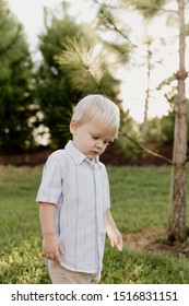 Portrait Of Cute Handsome Blond Little Kid Boy In Colorful Striped Button Down Shirt Walking Outside In The Grass Watching The Sunrise