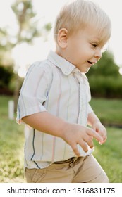 Portrait Of Cute Handsome Blond Little Kid Boy In Colorful Striped Button Down Shirt Walking Outside In The Grass Watching The Sunrise