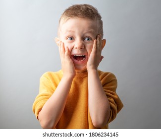 Portrait of a cute handsome European child on a gray background. Children's emotions-surprise, delight, wow. Hands to face. A 6-year-old boy grimaces. A beautiful and happy child.