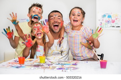 Portrait cute happy father and children painting   having fun  They are showing their hands painted in bright colors