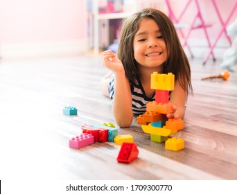 Portrait of a cute happy little preschool Hispanic girl playing alone with colorful construction blocks in her bedroom floor at home. Child Developing Motor Skills With Games Copy Space
