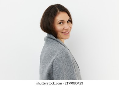 Portrait Of A Cute, Happy, Pleasant Woman Smiling Happily At The Camera While Standing In A Gray Coat On A Pale Background With An Empty Space For An Advertising Mockup