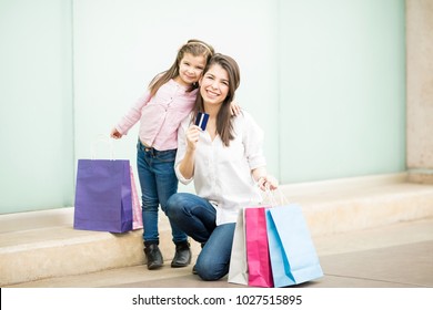 Portrait Of Cute Hispanic Mother And Daughter Outside A Shopping Center With Lots Of Shopping Bags And Showing Credit Card