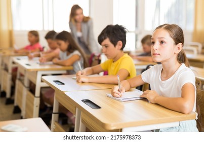 Portrait of cute intelligent schoolgirl who writing exercises at lesson in primary school