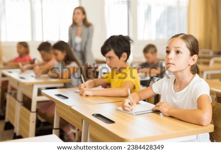 Portrait of cute intelligent schoolgirl who writing exercises at lesson in primary school