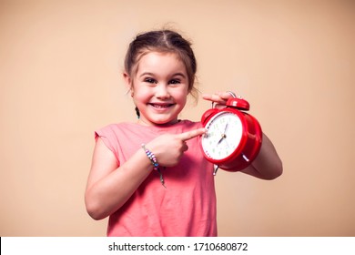 A Portrait Of Cute Kid Girl Pointing At Alarm Clock. Children And Time Management Concept