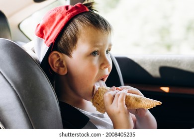 Portrait Of A Cute Kid In A Red Cap Eating Ice Cream In A Waffle Cone While Traveling In A Child's Chair In The Car. Little Boy Licking Ice Cream