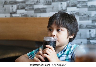 Portrait Of Cute Kid Sitting On Table With Cold Drink In Restaurant, Child Boy Drinking Soda Or Soft Drink With Straw, Child Boy Waiting For Foo In Cafe