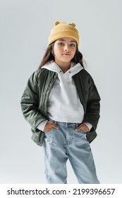 portrait of cute kid in yellow beanie hat and stylish autumnal outfit posing with hands in pockets isolated on grey - Shutterstock ID 2199396657