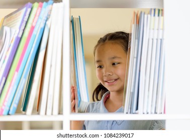 Portrait Of A Cute Little 10 Year Old Girl. Asian Children Choosing A Book In The Library. Happy Smiley Kids Or Pupils Looking At The Books. Education,creativity And Promotion Of Reading Concept.