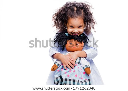 Portrait of a cute little african american girl hugging doll, isolated on white background