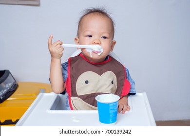 Portrait Of A Cute Little Asian 18 Months / 1 Year Old Toddler Baby Boy Child Eating Yogurt. Dirty Face Of Funny Kid. Smiling Toddler Eating With A Stained Face, Self Feeding Concept