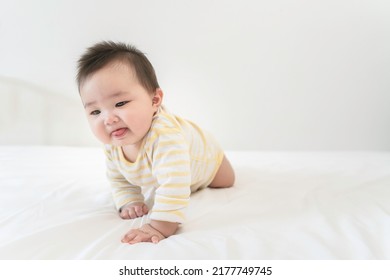 Portrait of cute little asian baby girl wearing bodysuit lying on white beedsheets at home. Cute infant child crawling on bed in the bedroom. Selective focus, free copy space. Childcare Concept. - Shutterstock ID 2177749745
