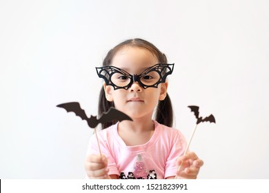 Portrait Cute Little Asian Girl 3 Year Wear Bat Glasses And Holding Sticky Paper Bat For Her Costume. Concept Halloween Kid, Fancy Halloween And New Year Party, Happy Kid. Celebrities And Education.