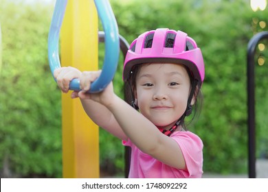 Portrait Cute Little Asian Girl 3 Year Old Smile And Hanging On The Monkey Bar In Playground. Asia Kid Wearing Helmet To Protect Her Head. Concept Playing Outdoor, Adventure Activity, Safety And Fun.