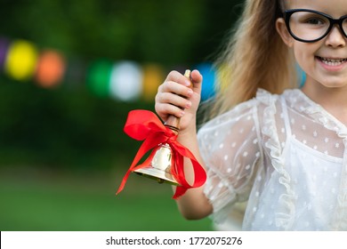 Portrait von süßem kleinen blonden Mädchen mit Schwänzen und Brillen in der Schule Uniform Ringelgoldschule Glocke auf Flaggenhintergrund.Kopienraum.