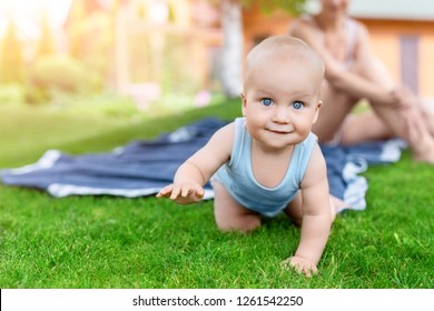 Portrait of cute little caucasian boy having fun in garden with mother. Child crawling on green grass lawn during walk with mom in yard. Happy childhood and baby healthcare.