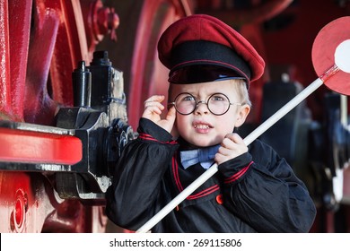 Portrait Of A Cute Little Child Boy With Annoyed Facial Expression As Nostalgic Railroad Conductor And Metal-rimmed Glasses, Cap And Signaling Disk/Upset Little Railroad Conductor