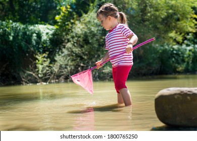 Portrait of a cute little girl 3-4 years old fishing with a net in the river on a Sunny day. Exploring nature, travel, family vacation