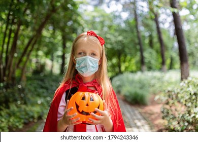 Portrait of cute Little Girl in costume of red hat in the park. Happy Halloween during coronavirus covid-19 pandemic quarantine concept. Kid wearing medical mask