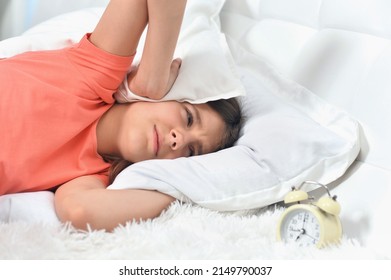 Portrait Of Cute Little Girl Covering Head Trying To Sleep In Noisy Room