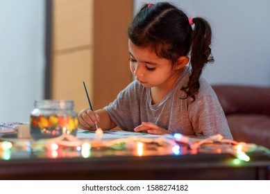 Portrait Of Cute Little Girl Drawing At Home With Christmas Decorations. Real Life, Happy Moments, Cozy Home.