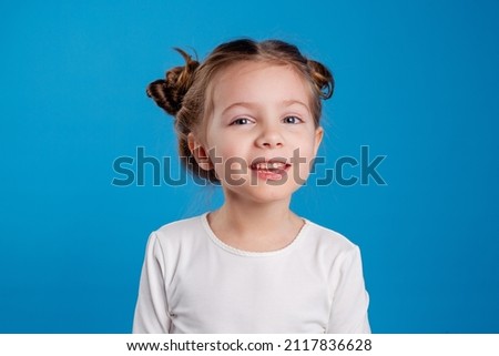 portrait of a cute little girl with a funny hairstyle in a white T-shirt. blue background. space for text. High quality photo
