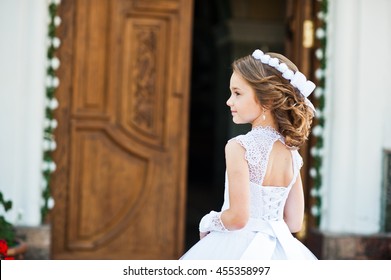 Portrait of cute little girl on white dress and wreath on first holy communion background church gate