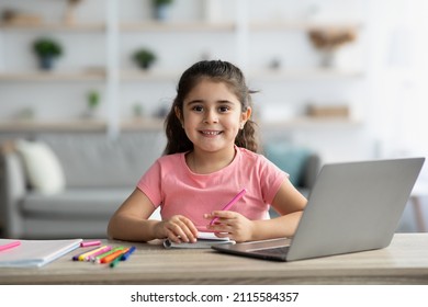 Portrait Of Cute Little Girl Sitting At Table With Laptop And Drawing In Notepad, Smiling Preteen Female Child Study Remotely With Computer At Home, Enjoying Online Education, Copy Space - Powered by Shutterstock