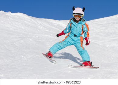 Portrait Of Cute Little Girl Skiing Downhill On A Sunny Day. Skier Wearing A Protective Crash Helmet And Ski Goggles. Copy Space For Text