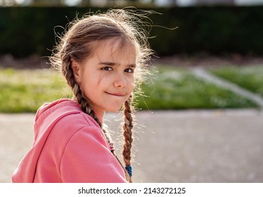 Portrait of cute little girl with sly look and backlit hair in spring park looking at camera. Child enjoying playing outdoors