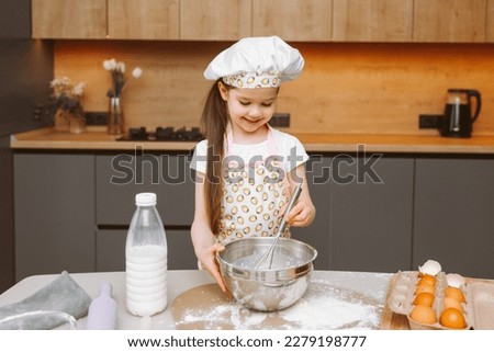 Portrait of a cute little girl standing in a modern kitchen and preparing dough.