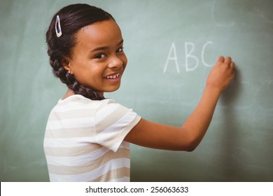 Portrait Of Cute Little Girl Writing ABC On Blackboard In The Classroom