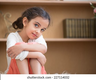 Portrait Of Cute Little Hispanic Girl Sitting On Carpet At Home