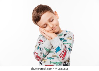 Portrait of a cute little kid standing with hands sealed pretending he is sleeping isolated over white background