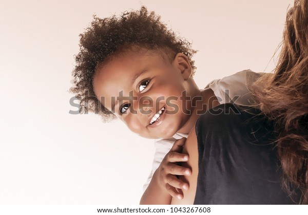 ベージュ白の背景に幸せなアフリカ系アメリカ人の家族 愛と団結のコンセプト 母親の肩の後ろから見るかわいい小さな笑顔の赤ちゃんのポートレート の写真素材 今すぐ編集