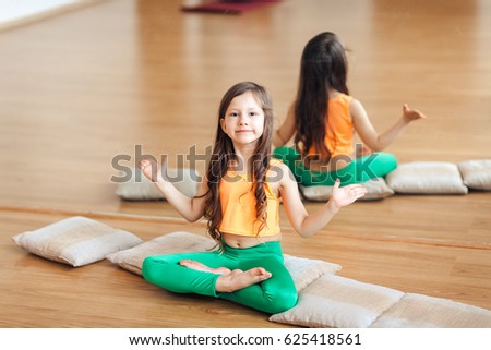 Portrait of a cute little smiling girl practicing yoga, in an orange suit