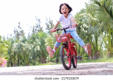 Portrait, A Cute Looking Asian Girl Aged 6 Years And Over, Wearing A White Shirt And Blue Pants. She Was Riding Her Favorite Red Bike, Playing Wildly In Different Poses. Both Legs Spread Confidently.