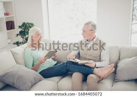 Portrait of cute married sweethearts holding printed book relax wear denim jeans trousers brown teal pullover shirt sit lie bare foot divan in room